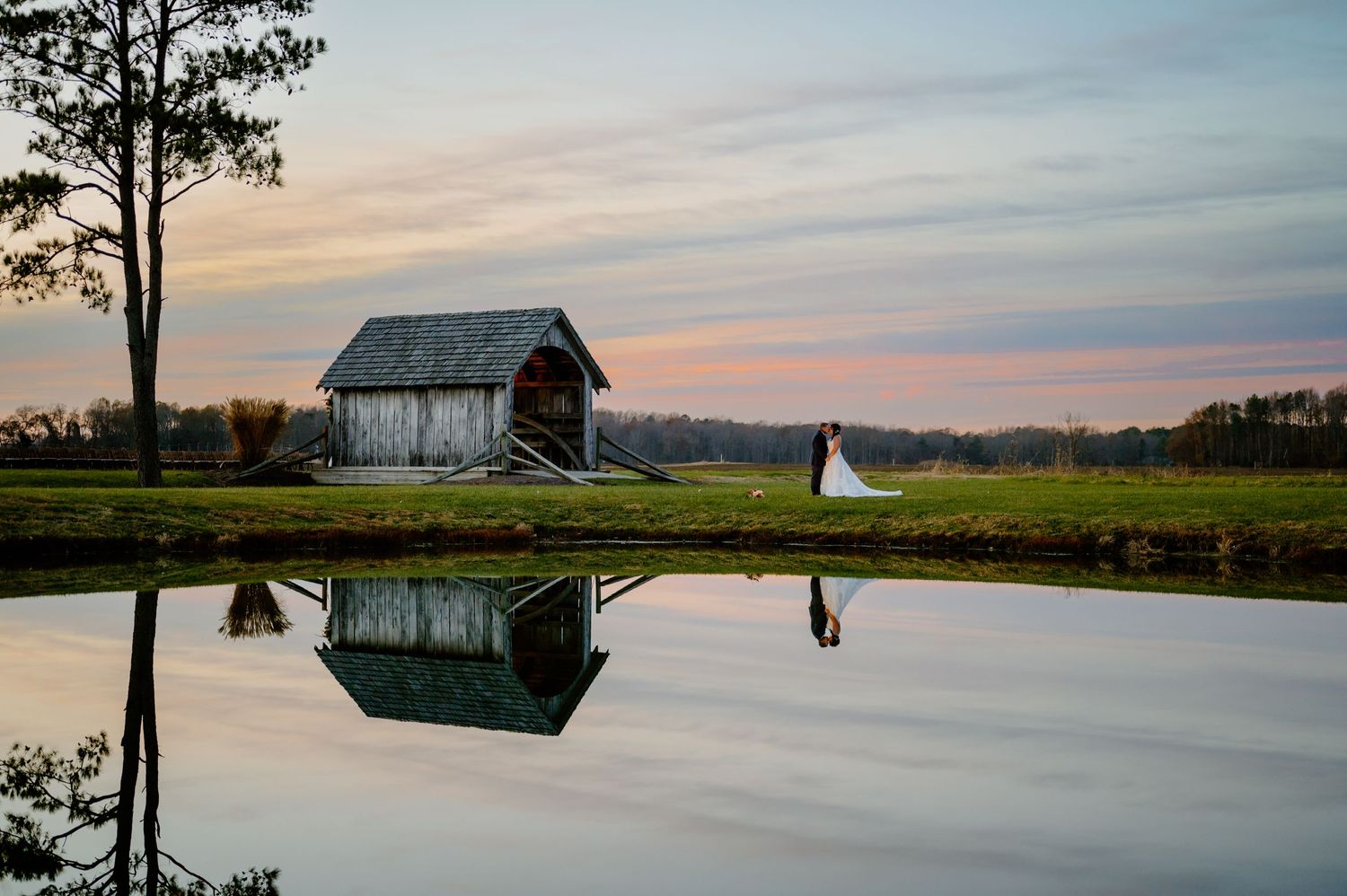 Bride and groom kissing under a gorgeous colorful sunset by a pond, near the Covered Bridge Inn in Lewes, Delaware.
