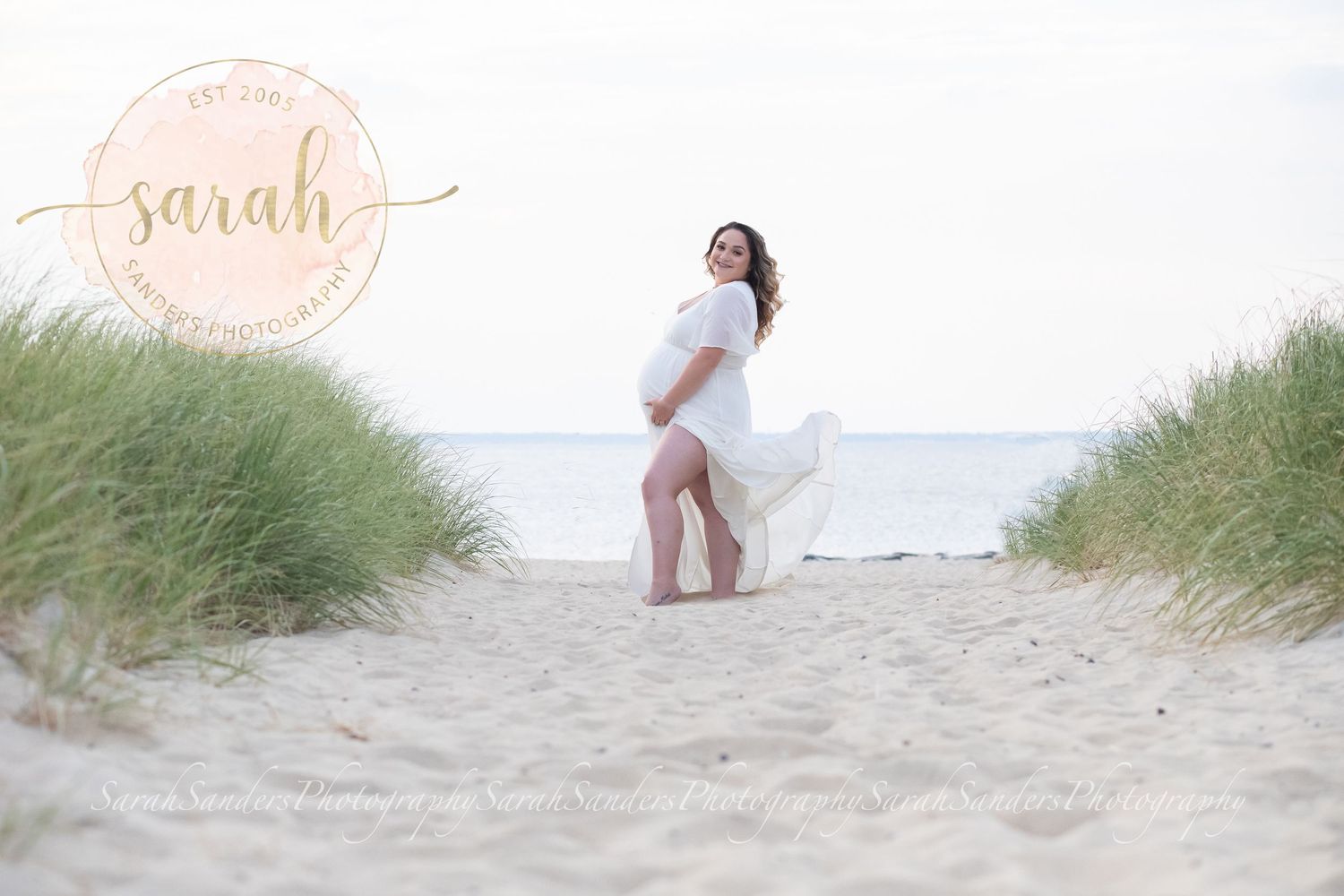 Pregnant woman stands on beach posed with flowing sheer