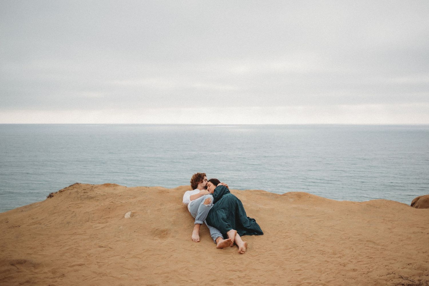A couple lays together on a cliff overlooking the beach.