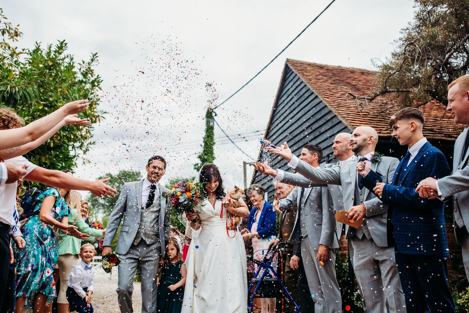 Wedding celebration with guests throwing confetti at a rustic outdoor venue.