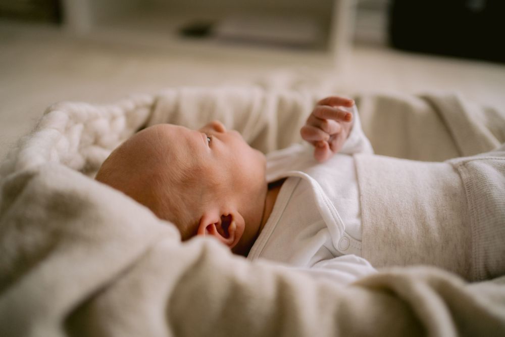 Sleeping baby in white clothing nestled in soft bedding.