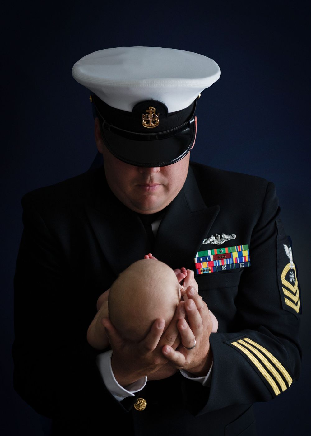 Navy service member in dress uniform holding a small object against dark background. Newborn Photography Batavia Cincinnati Ohio