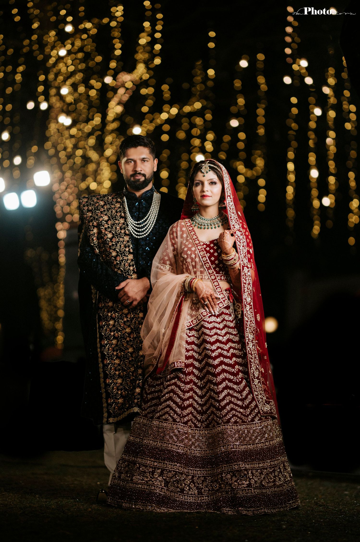 Elegant wedding portrait with couple in traditional Indian attire against a backdrop of golden bokeh lights.