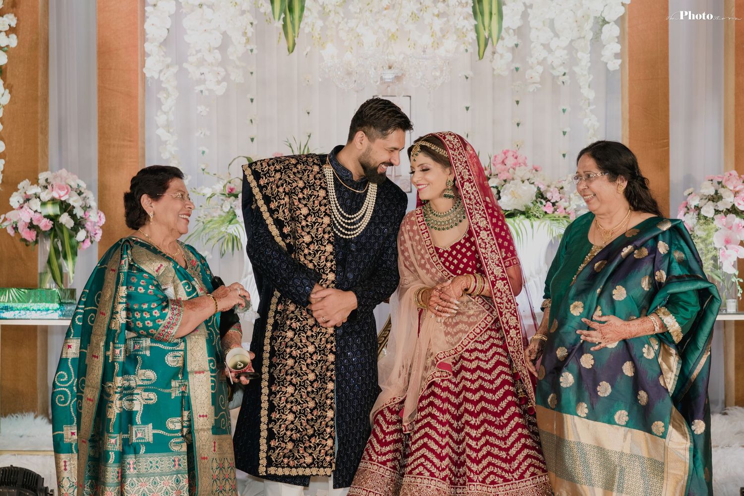 Wedding celebration with guests in colorful traditional South Asian attire against floral backdrop.