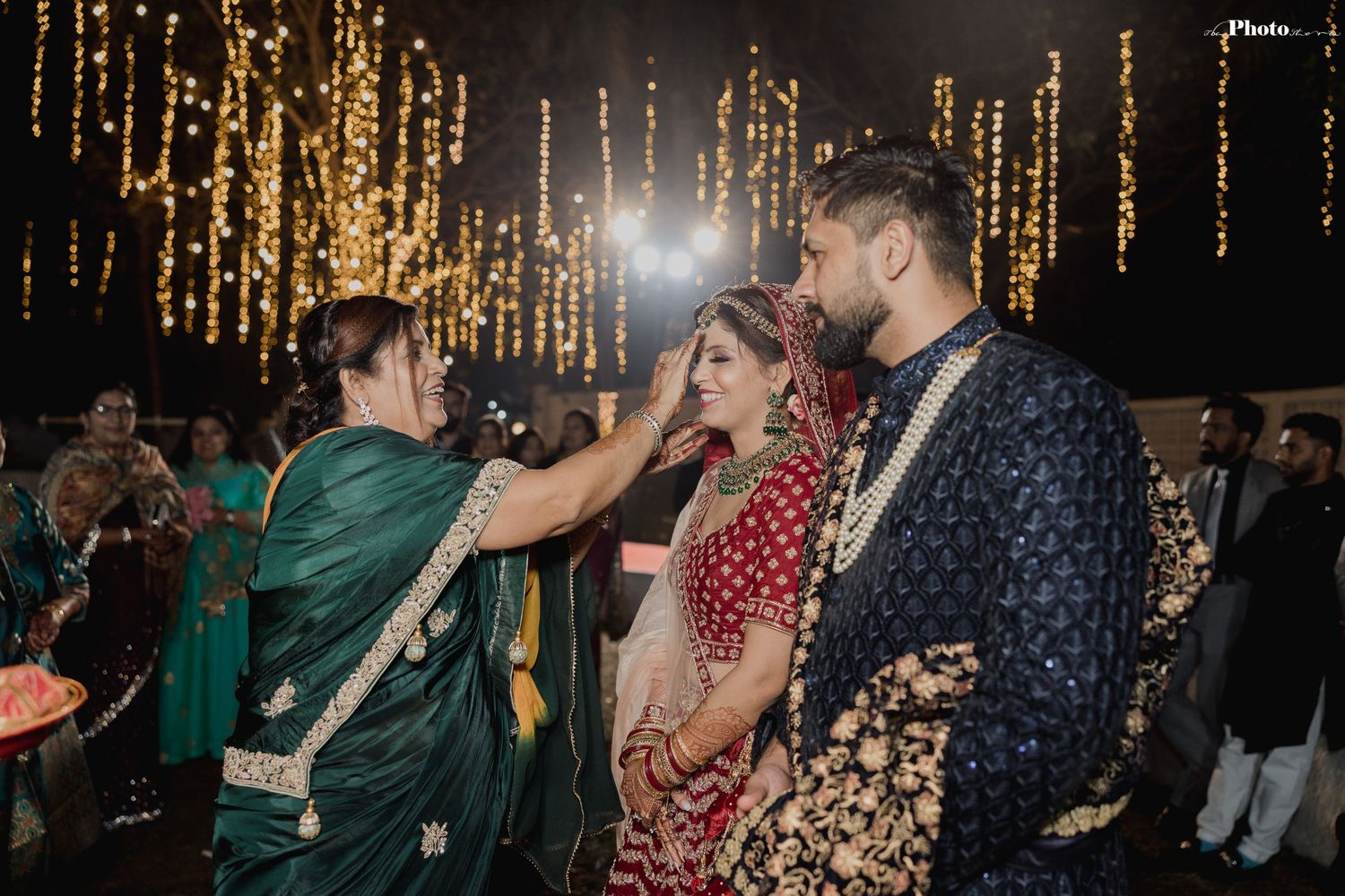 A couple in traditional Indian wedding attire share an intimate moment under sparkling golden lights.