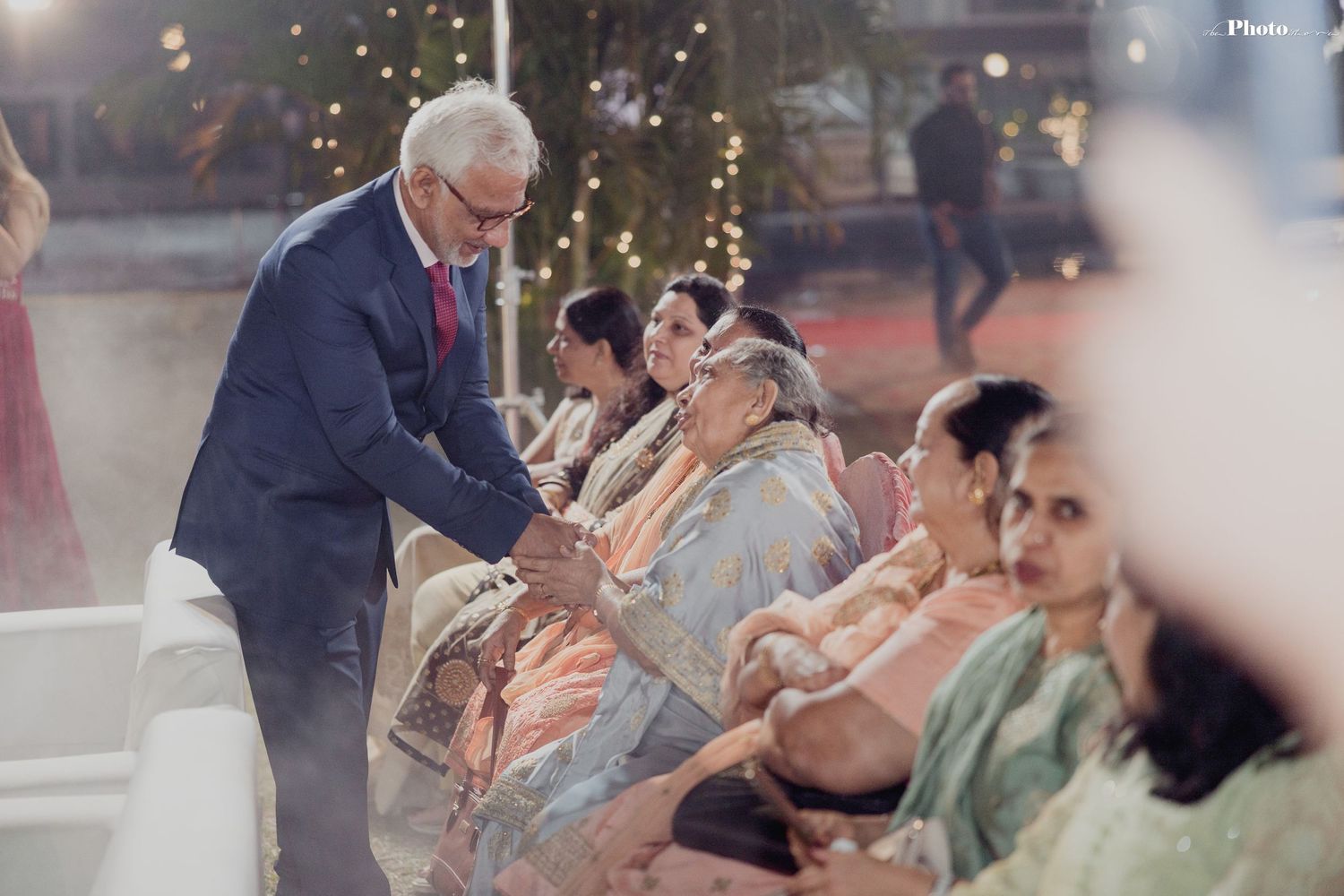 Wedding guests seated in formal attire at an indoor celebration venue with warm lighting.