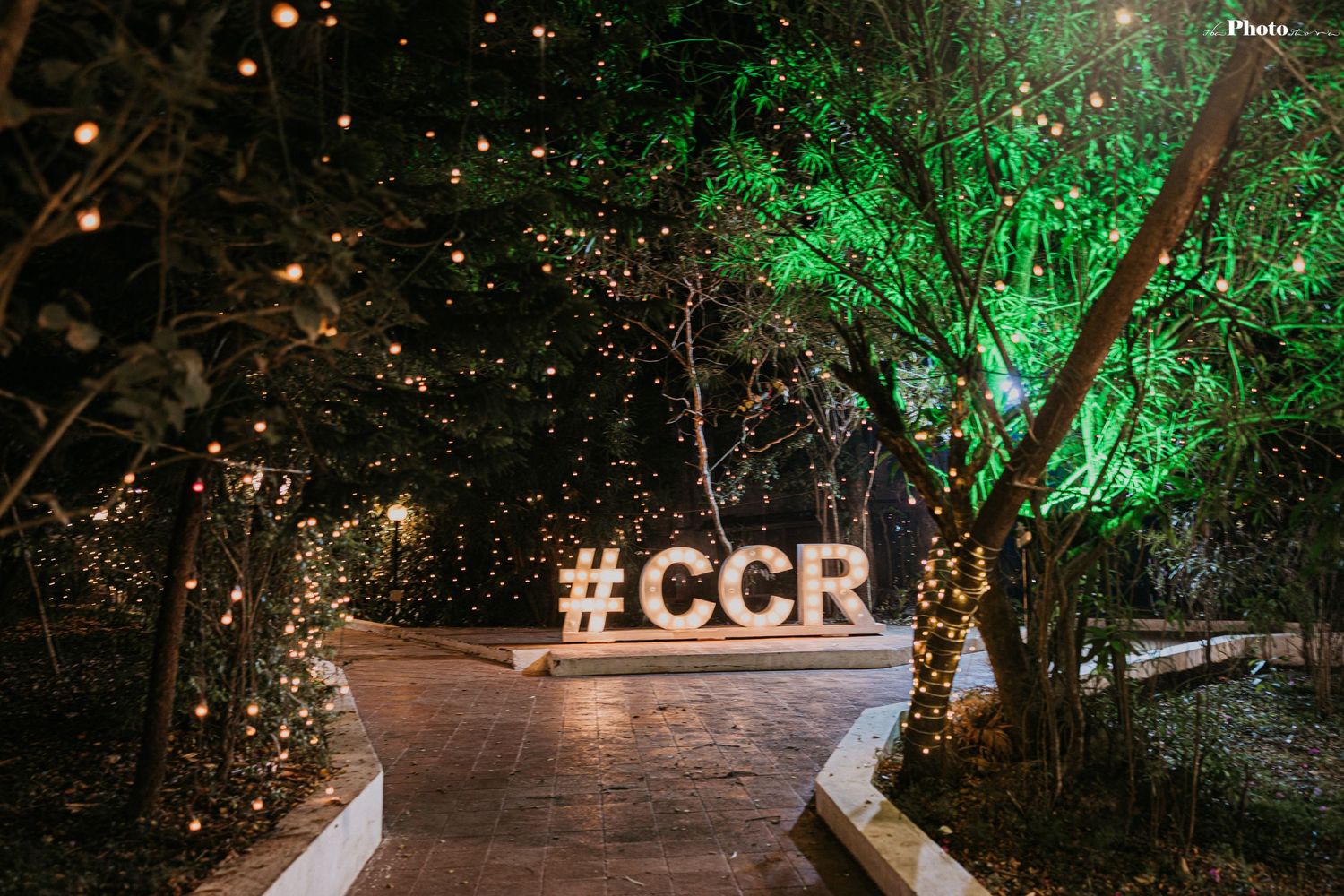 An illuminated outdoor wedding venue with #CCR sign and trees lit with green lights.