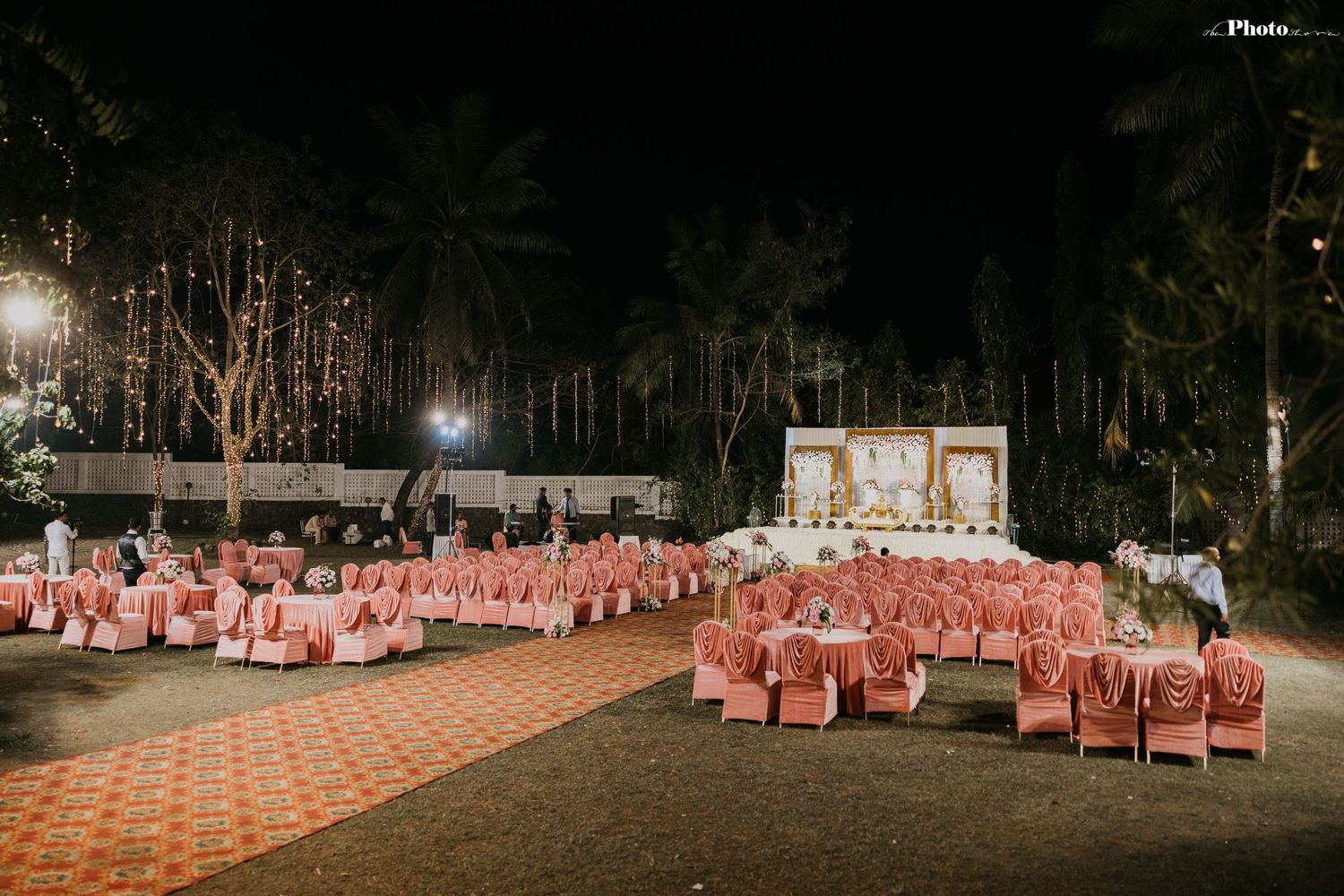 An outdoor wedding venue with coral-colored chairs arranged theater-style under evening lights.