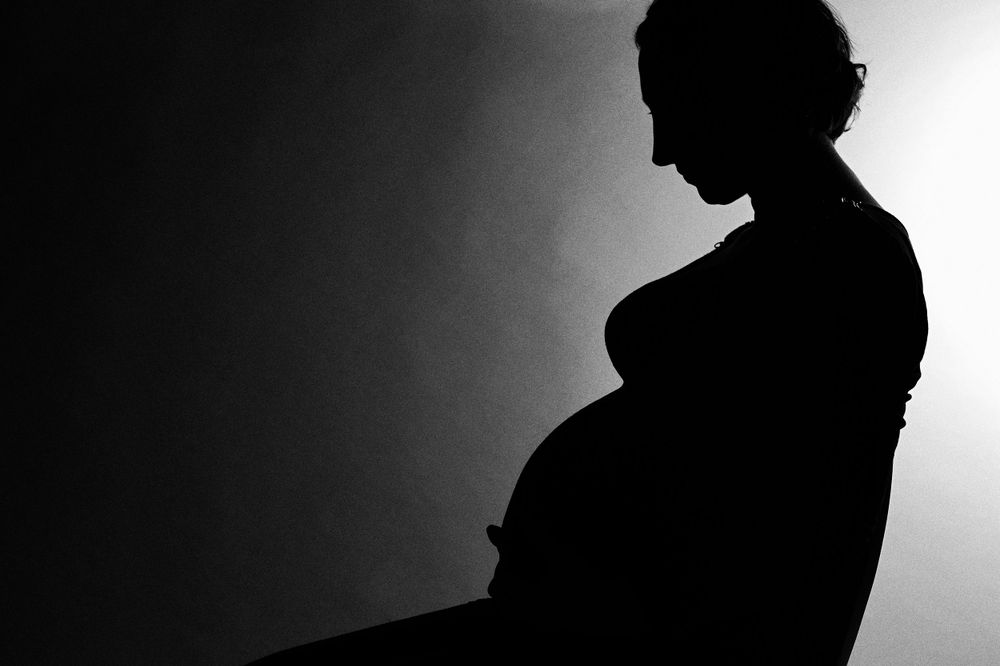 Side profile silhouette of pregnant woman against light background.