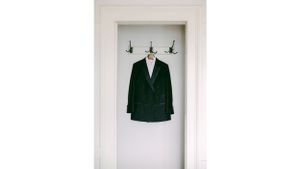 Dark green suit jacket hanging on white wall with hooks.