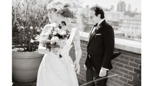 Black and white wedding photo of couple on rooftop with cityscape backdrop and floral bouquet.