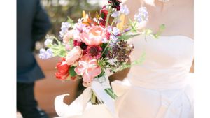 Vibrant pink and coral flower bouquet against white wedding dress fabric.