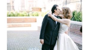 Intimate wedding couple portrait against brick wall and garden backdrop.