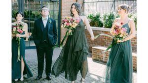 Wedding party in dark green dresses poses with groom outdoors.