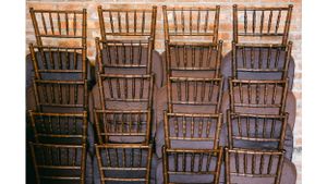Rows of stacked wooden Chiavari chairs against a wall.