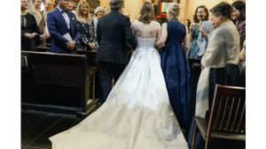 Elegant white wedding dress with full skirt shown from behind during wedding ceremony.