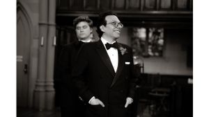 Two formally dressed individuals standing in classical architectural setting.