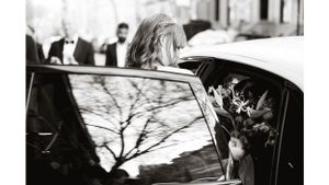 Black and white photo of person entering car with flowers.