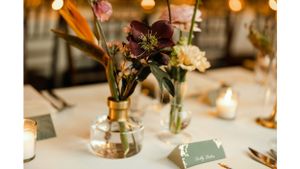 Wedding table centerpiece with delicate flowers in glass vases and candlelight.