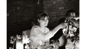 Bride reaching across an elegantly set dinner table with glowing candles and floral arrangements.