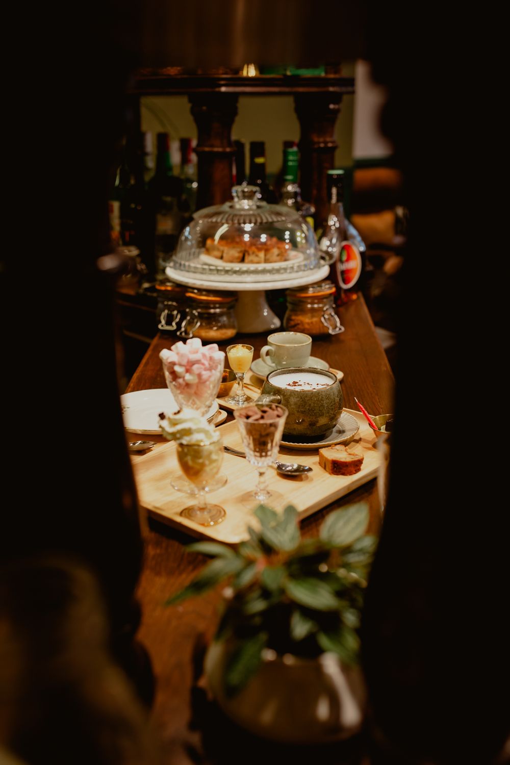 Dark and moody table setting with desserts, coffee cups, and a glass cake dome in a restaurant.