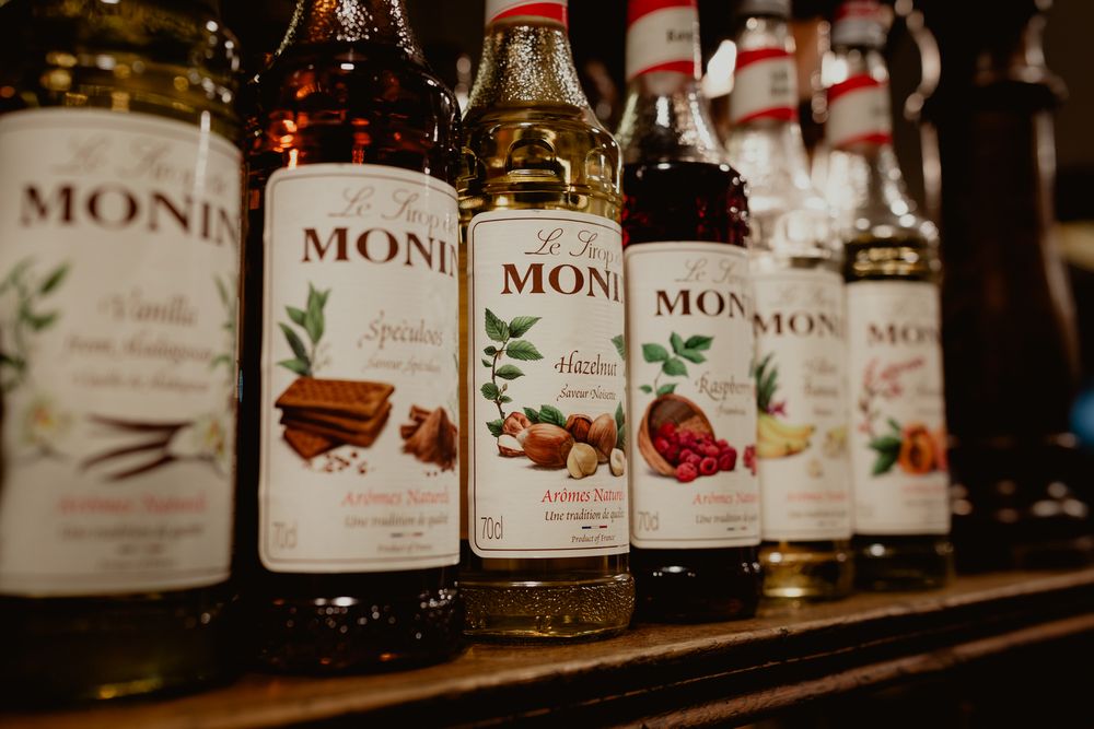 Row of Monin flavored syrup bottles displayed on a bar shelf.