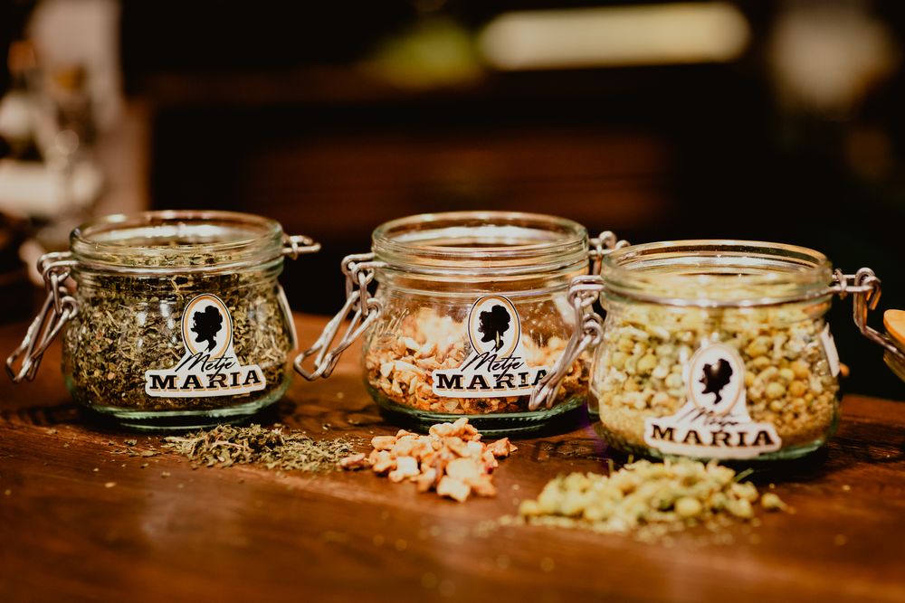 Three glass jars containing different botanical ingredients for gin making on a wooden surface.