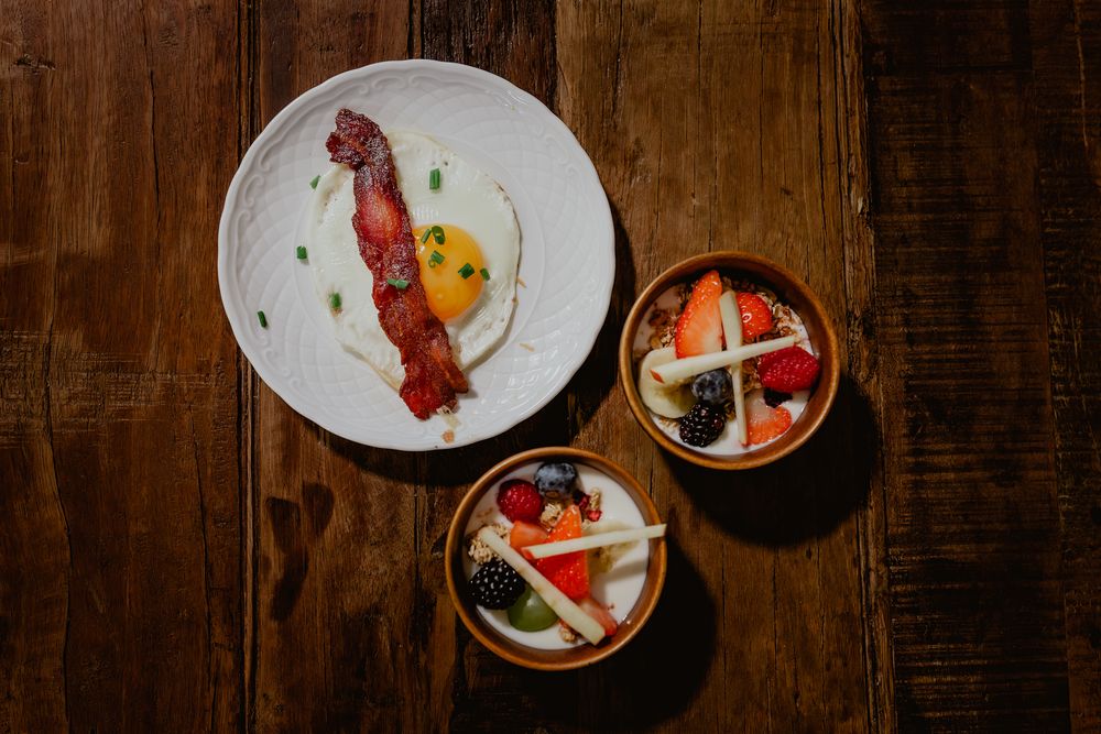 Elegant plated breakfast with bacon, eggs and side dishes on dark wooden table.