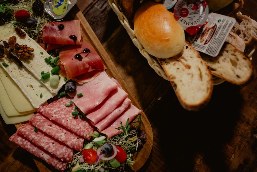 Charcuterie board with sliced meats, bread and garnishes on dark wooden surface.