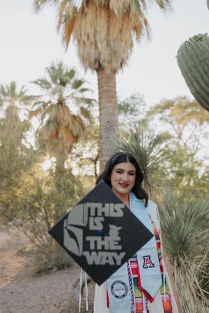 Graduate holding decorated graduation cap with 'This Is The Way' message.