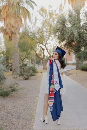 Graduate in blue graduation gown walking through desert landscape.