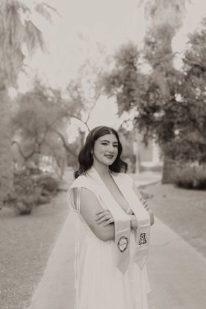 Black and white graduation portrait with graduate wearing white dress and stoles.