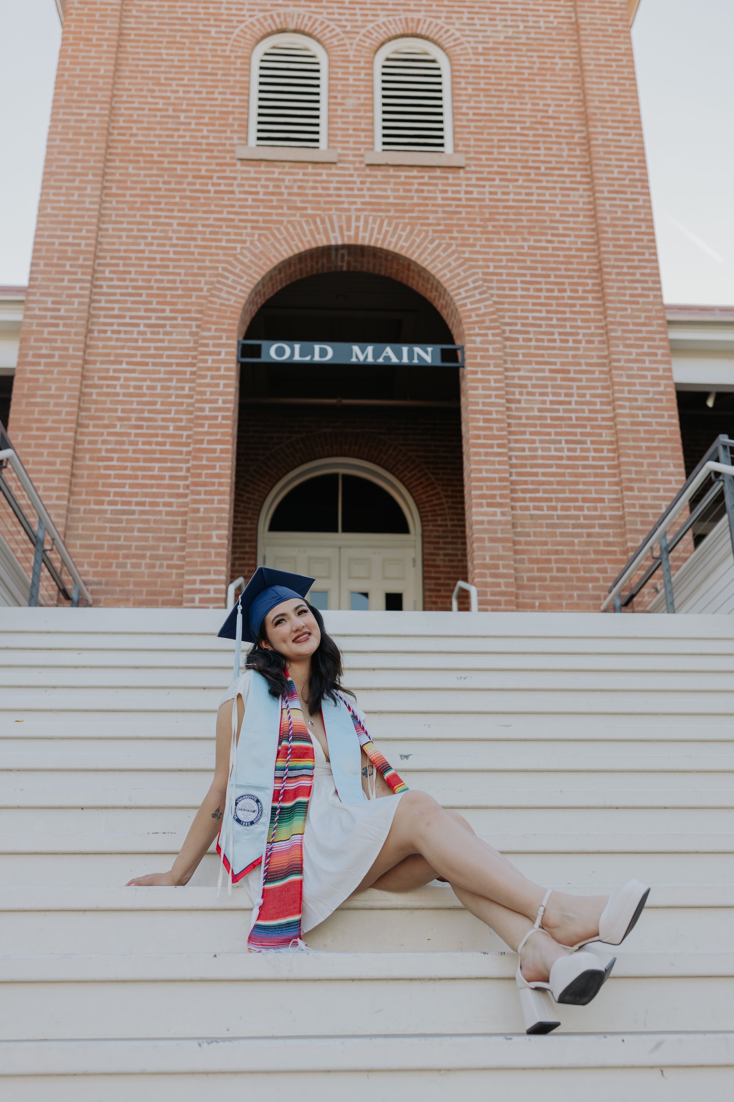 Graduate posing on the steps of Old Main building in graduation regalia.