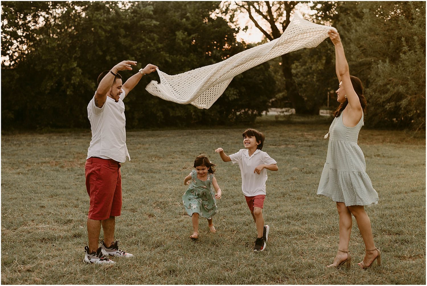 Family creates a tent-like structure with white fabric while children run underneath.