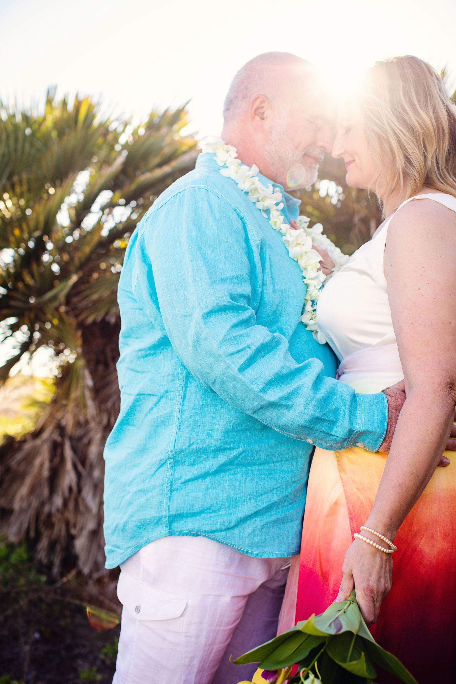 A romantic beach portrait of a couple wearing leis against a tropical backdrop.