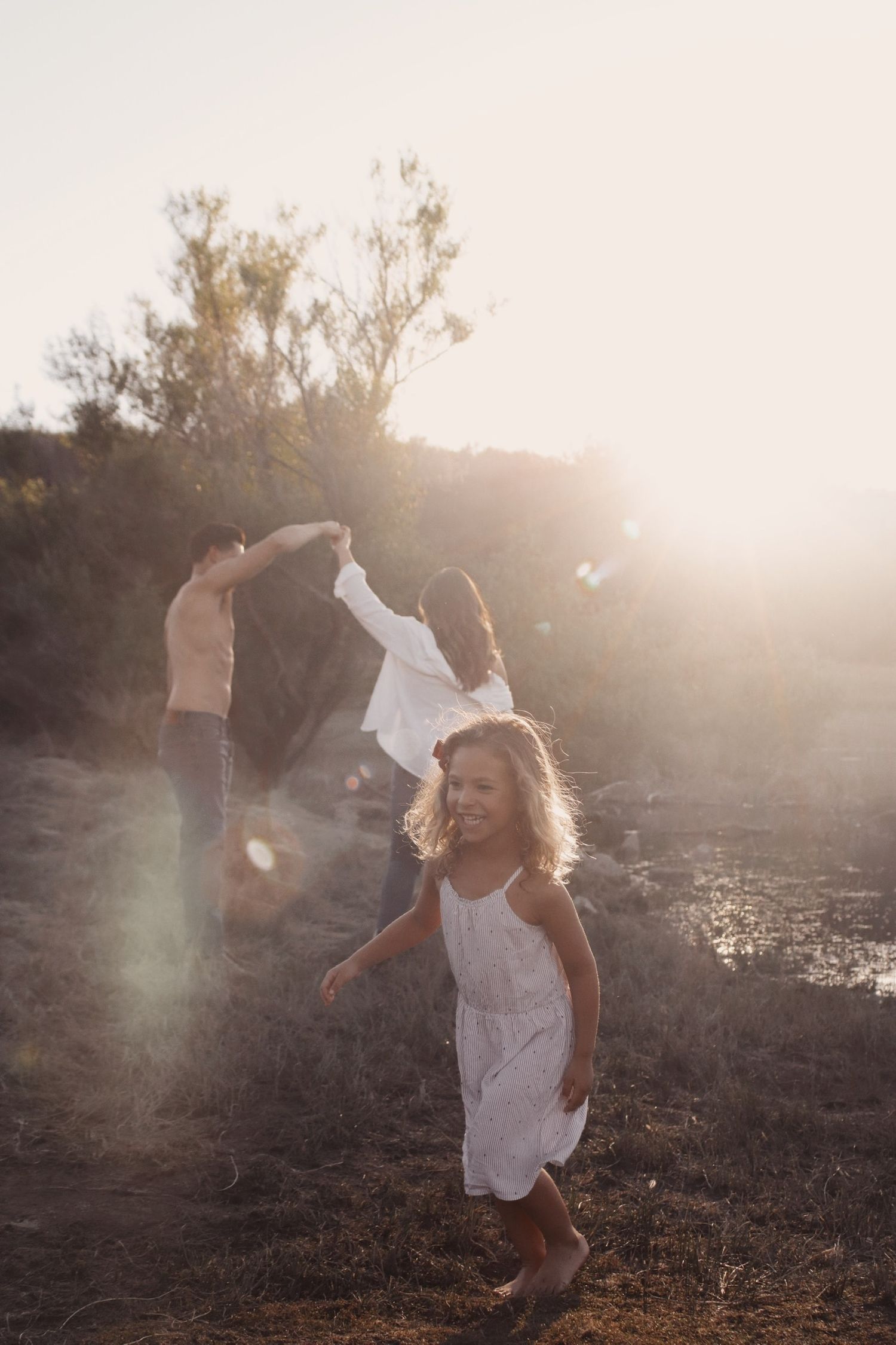 mother and father dancing with daughter in the dreamy sunlight