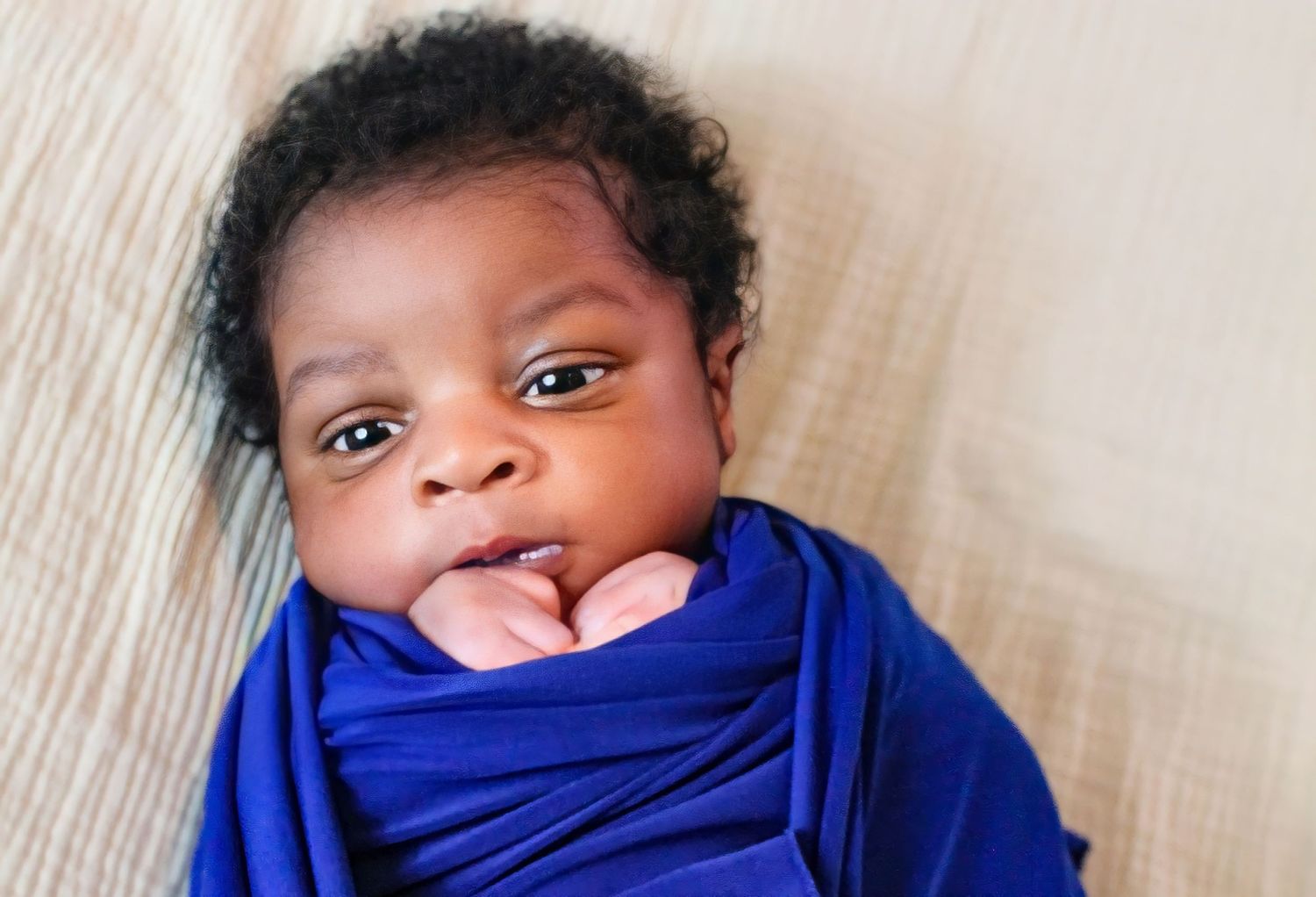 Baby wearing blue wrap looks at camera with curious expression.
