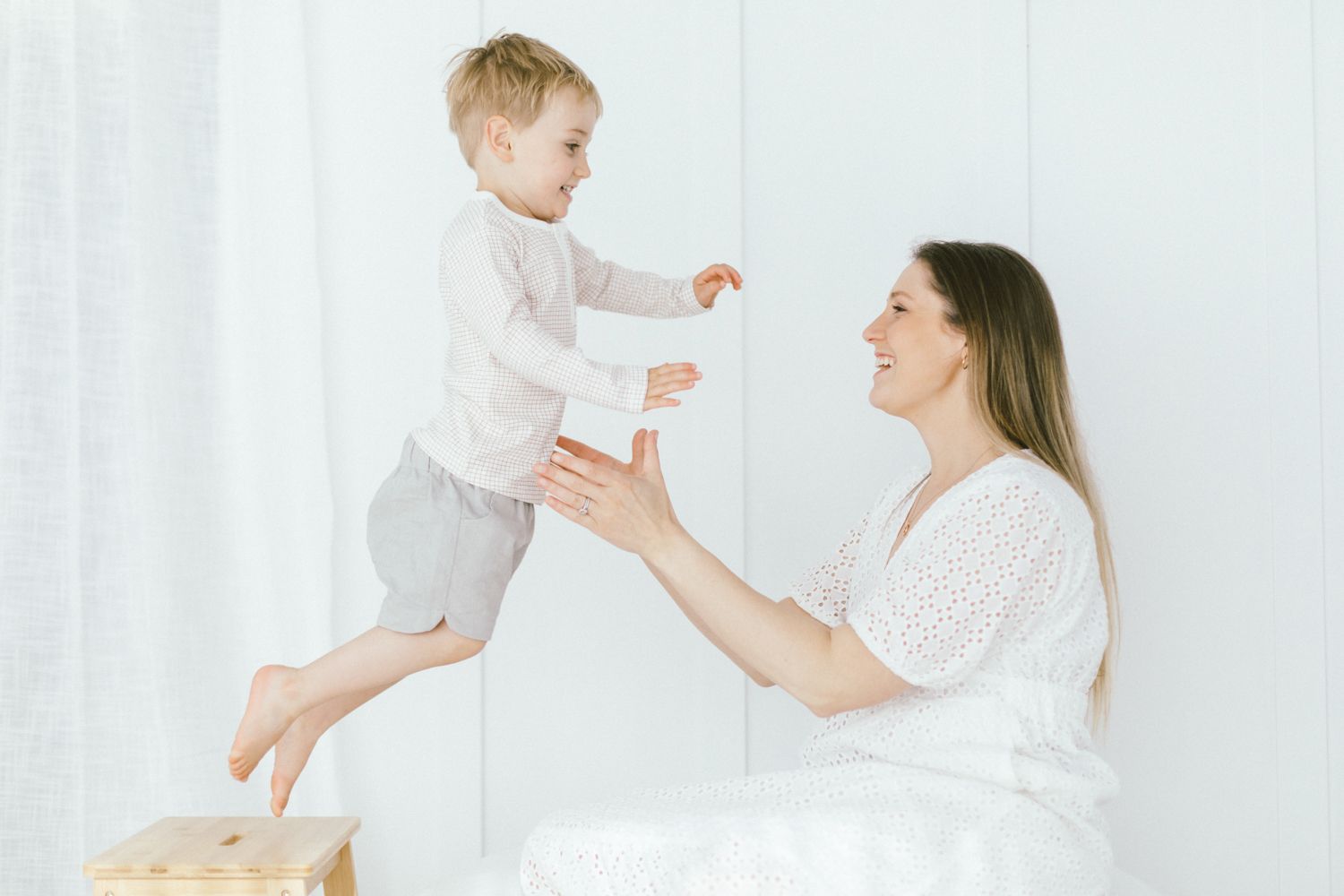 Family plays and laughs together on white bedding in a bright studio setting.
