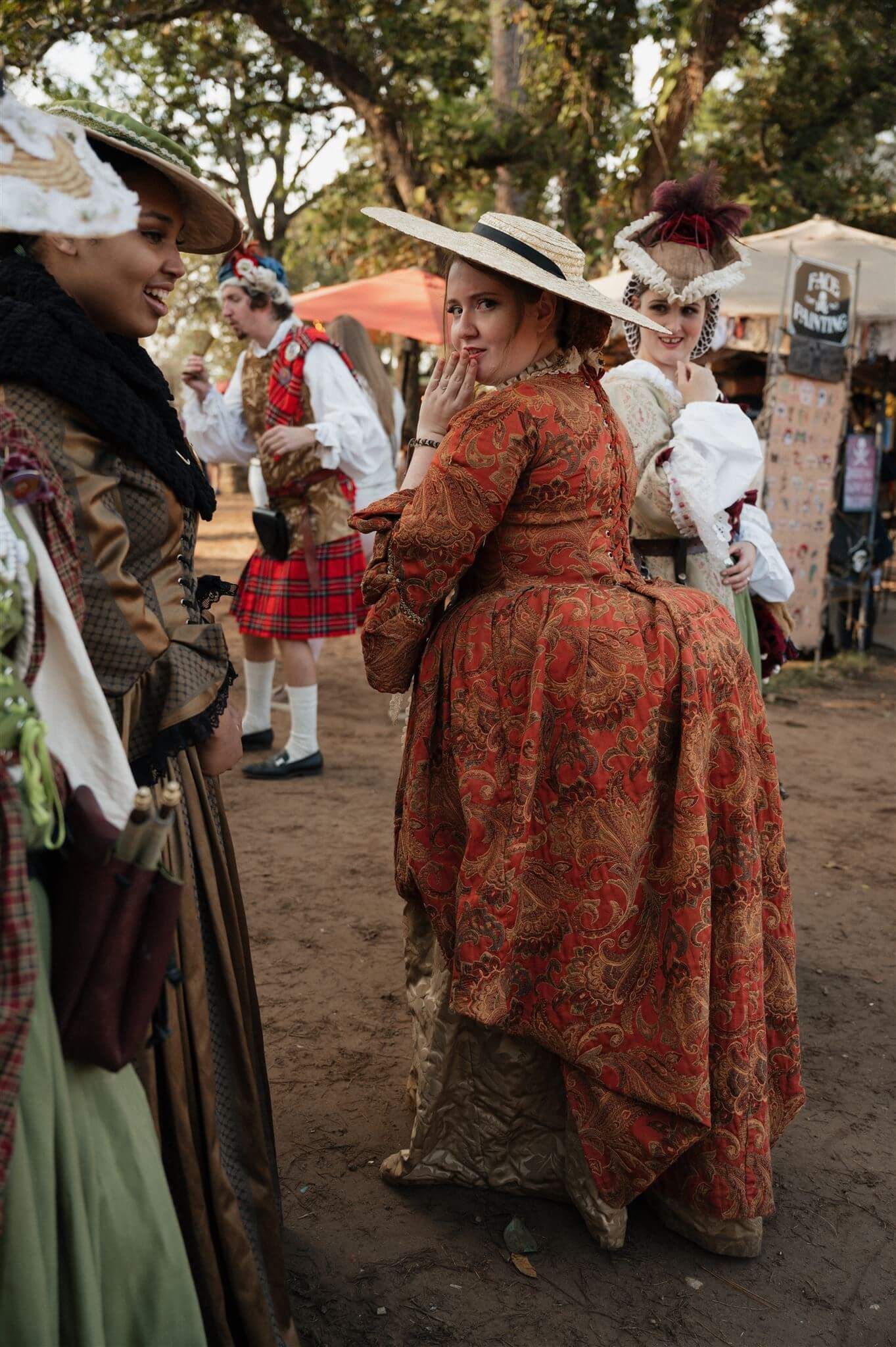 People in ornate historical costumes socializing at an outdoor renaissance festival.