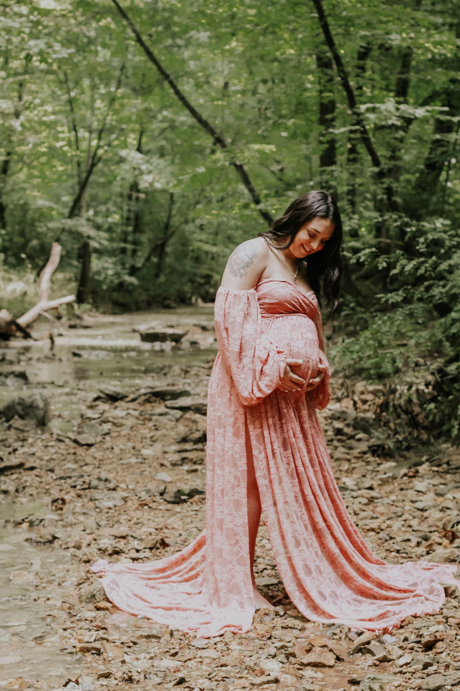 Woman in coral flowing dress posing gracefully in wooded setting.
