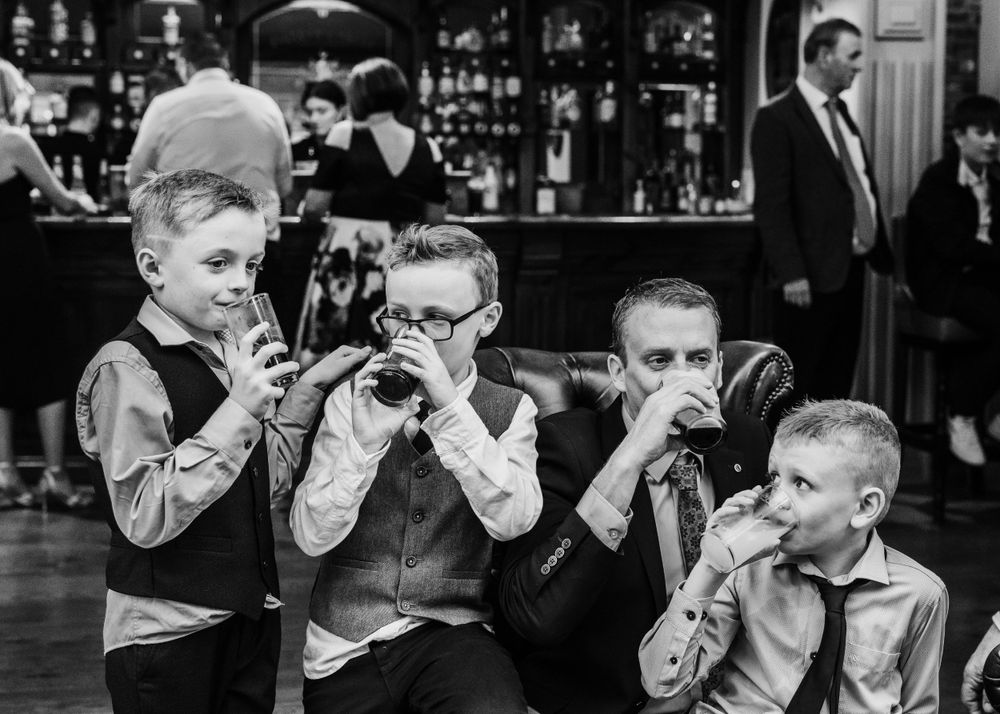 Young boys sitting at a bar drinking soda through straws in a classic black and white scene.