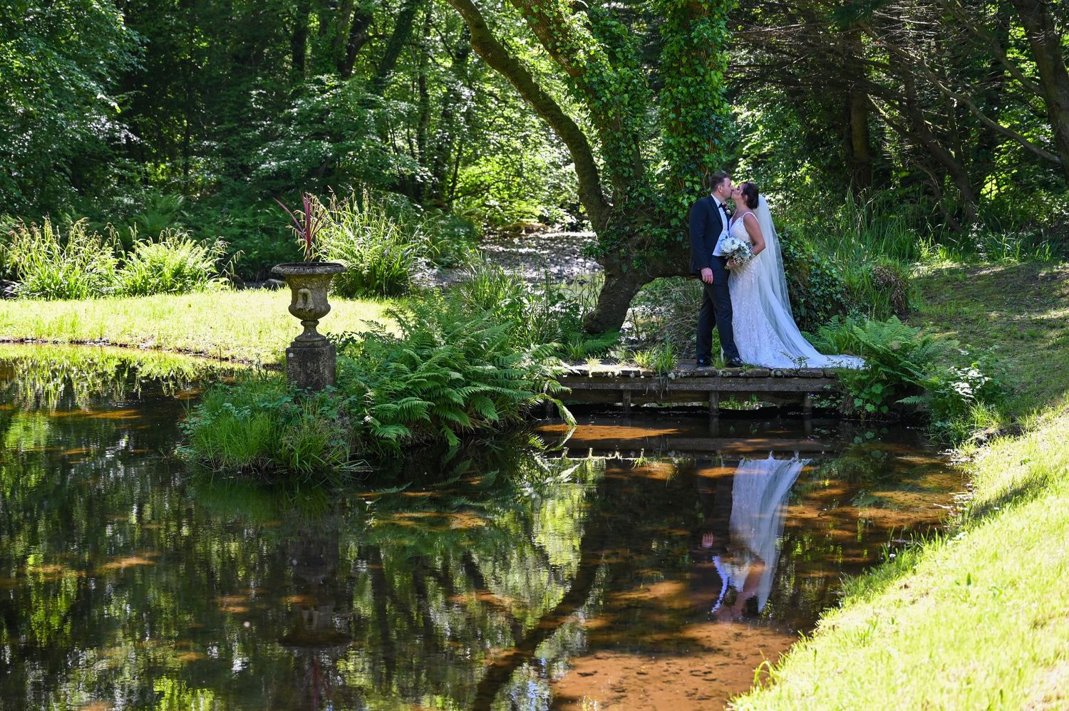 A romantic wedding photo of a couple reflected in a serene pond surrounded by lush gardens.