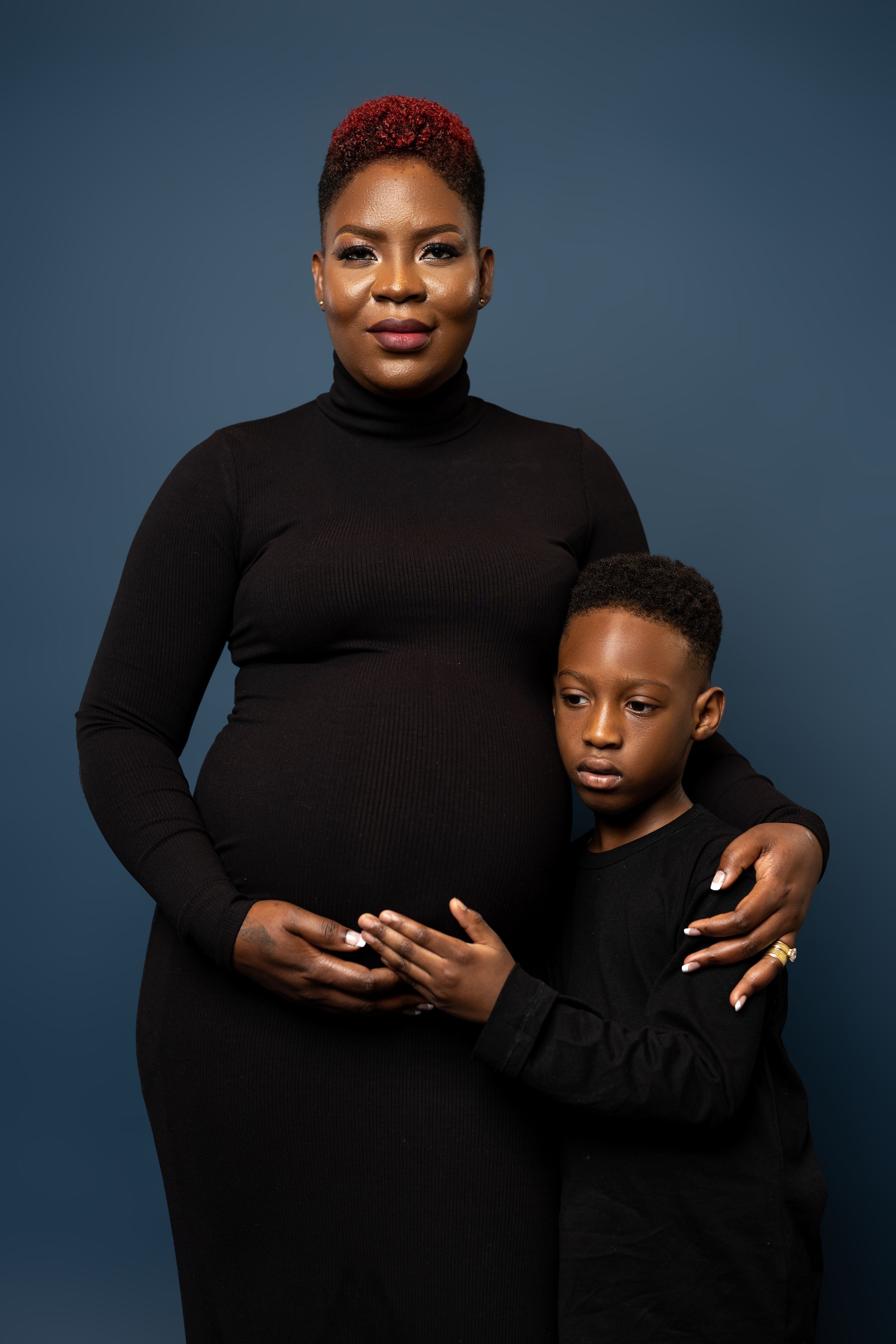 Studio portrait of pregnant woman and child in matching black outfits.