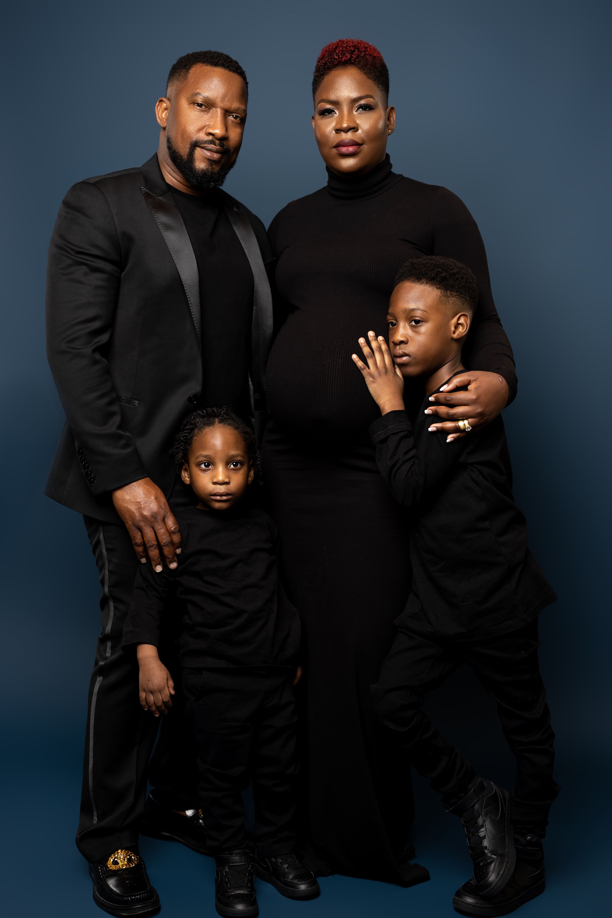 Studio family portrait with parents and children all wearing black against blue backdrop.