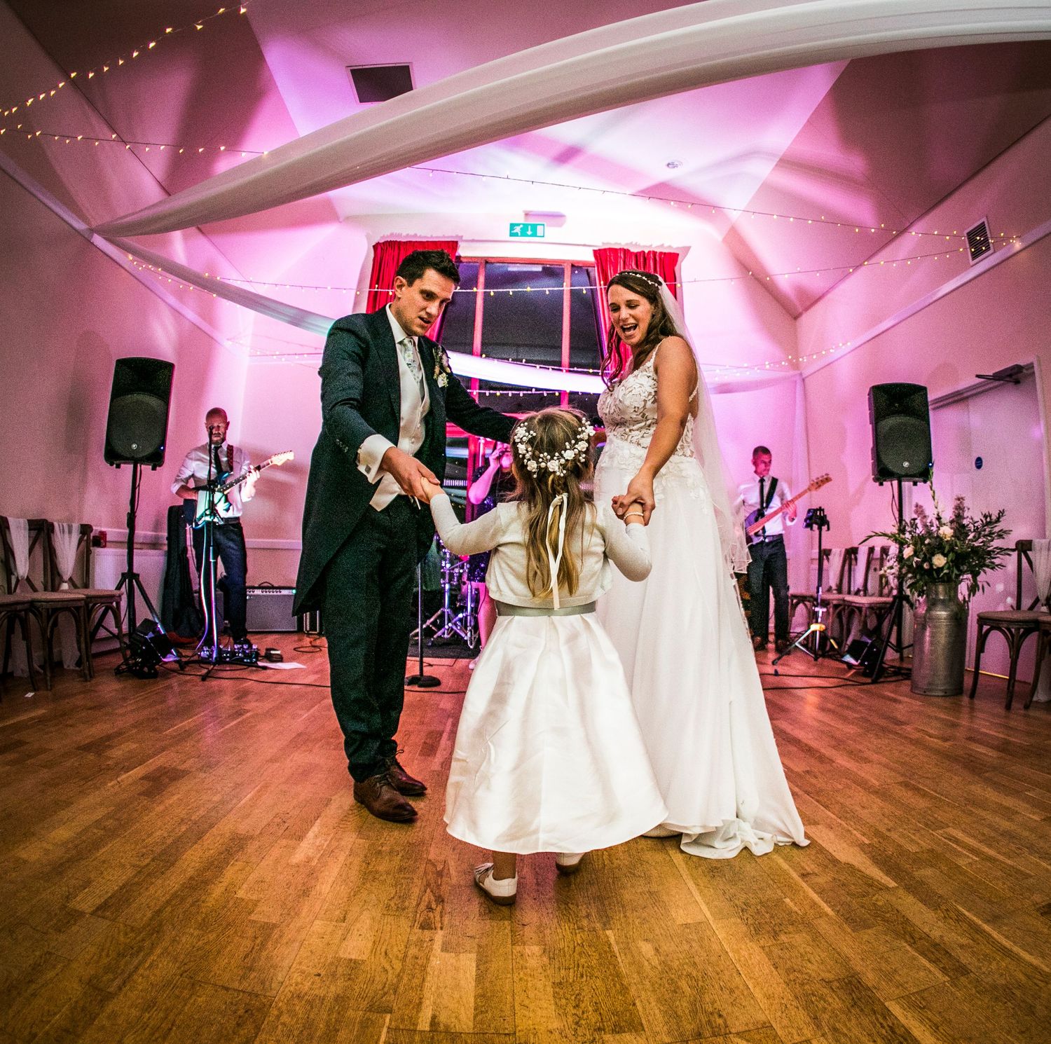 Wedding couple dancing on wooden floor under pink lighting at reception venue.