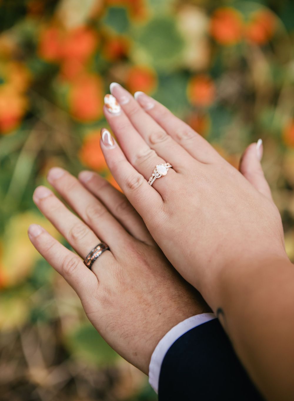 Close-up of wedding rings displayed on hands against blurred orange and green garden background.