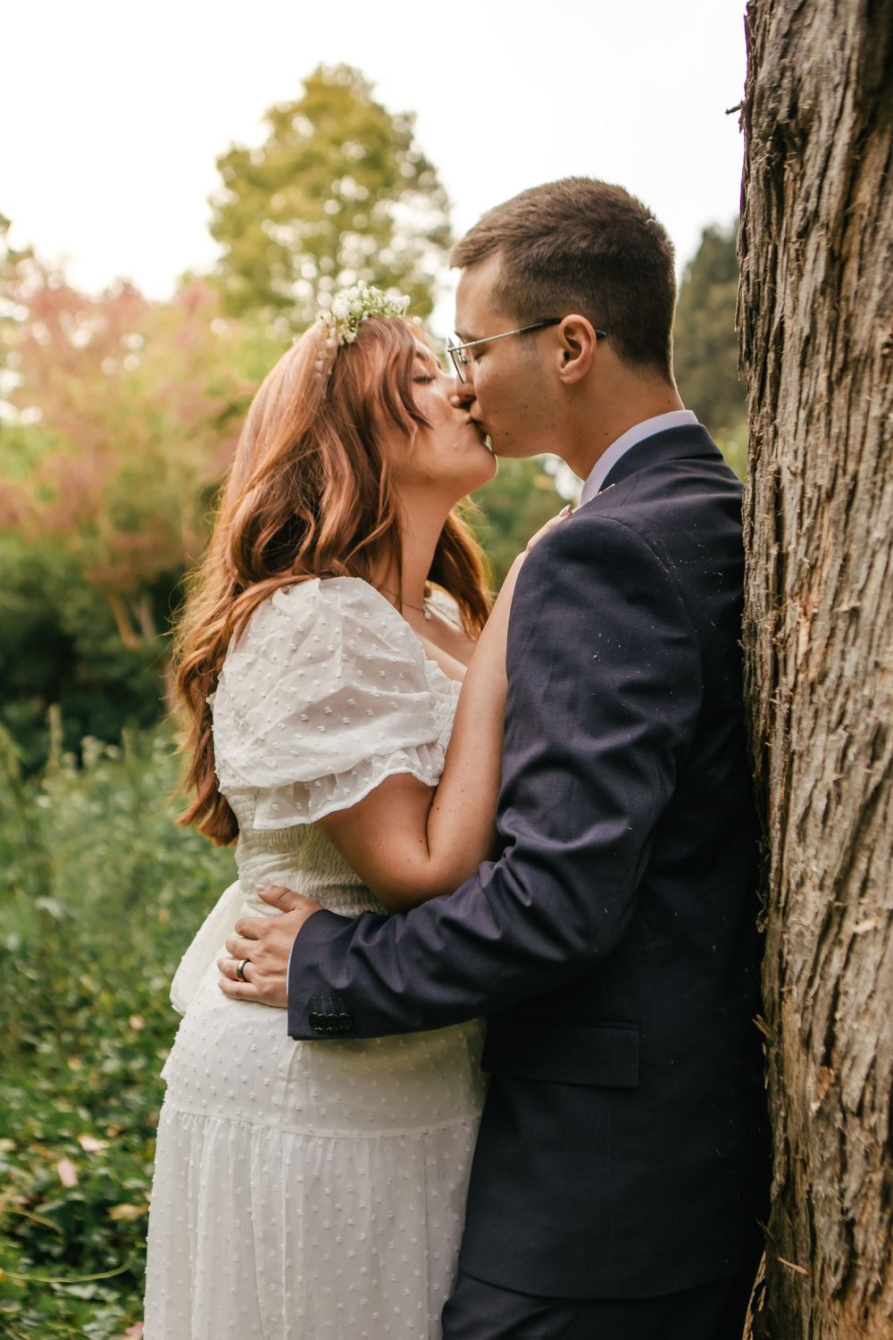 Romantic couple shares intimate moments against rustic tree trunks in a garden setting.