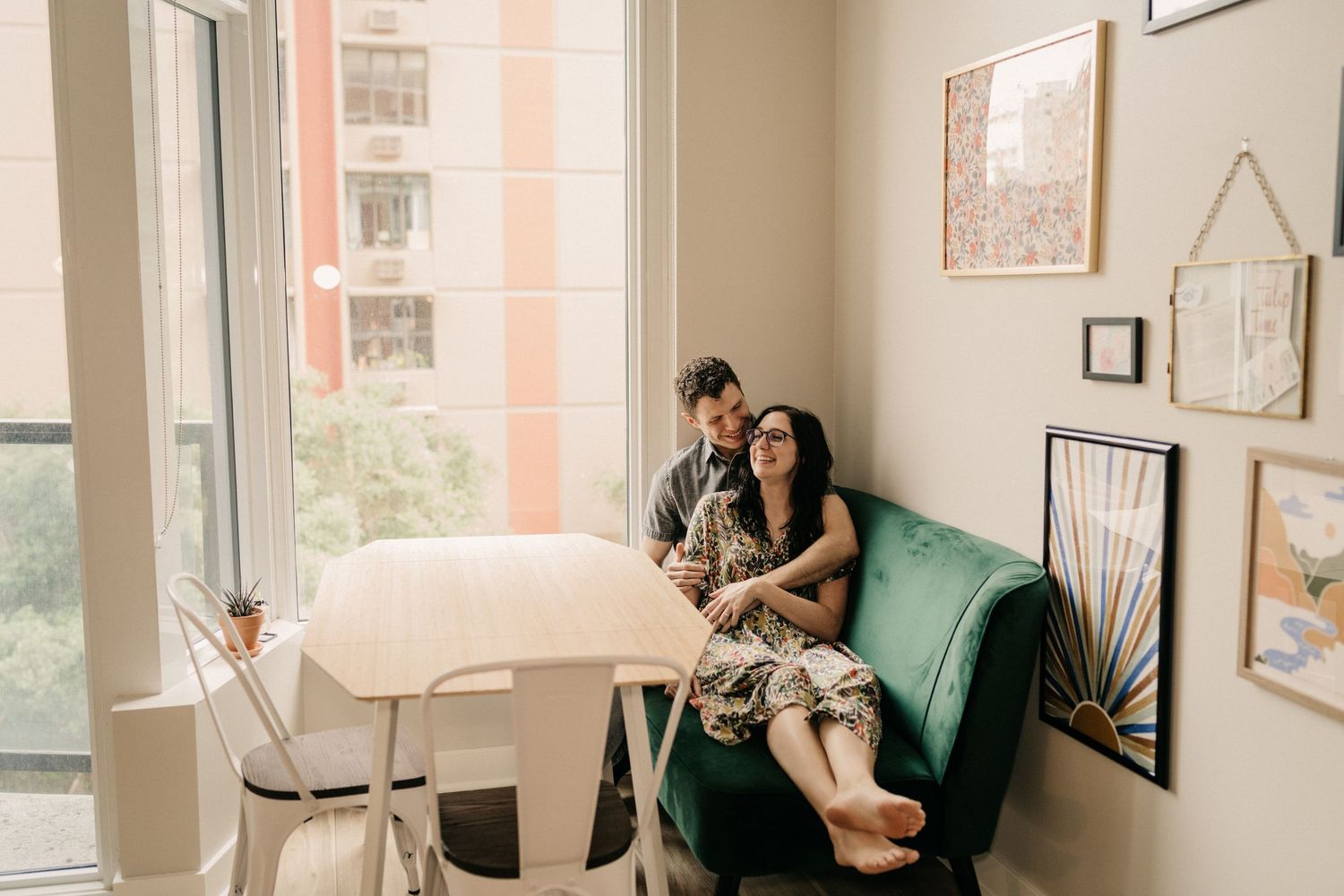 A couple sharing an intimate moment on a green velvet couch in a sunlit apartment.