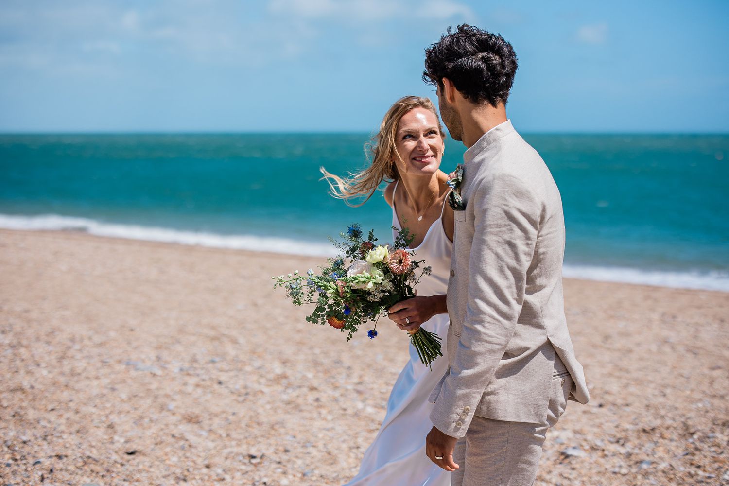 A bride smiles up at the groom, whilst taking a walk on the beach during their english seaside wedding reception in Devo