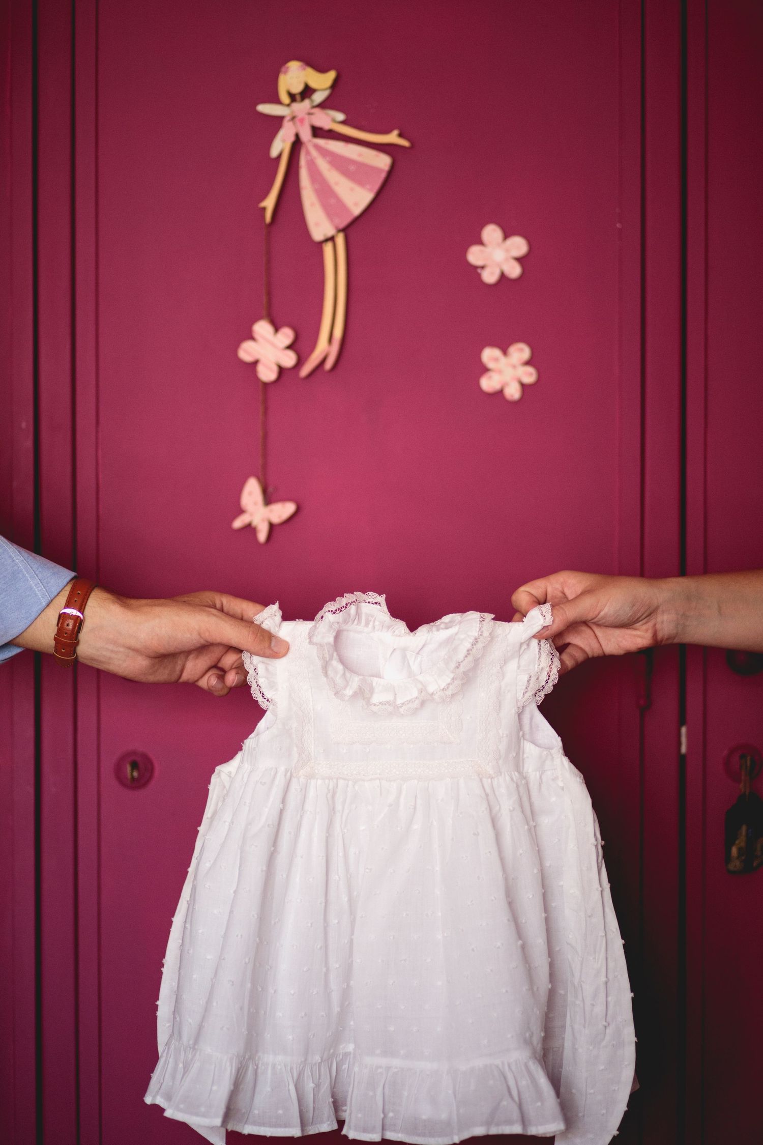 As mãos dos padrinhos a segurar o vestido de batizado da afilhada no momento da preparação em casa. Batizado em ovar